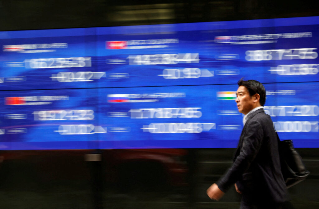 A passerby walks past an electric monitor displaying various countries' stock price index outside a bank in Tokyo, Japan. REUTERS/Issei Kato/File Photo